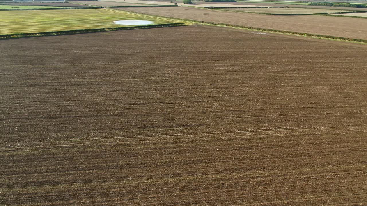 Aerial drone footage flying over a brown harvested field close to hedgerows and a farm track in North Yorkshire, UK on a beautiful, crisp autumn morning