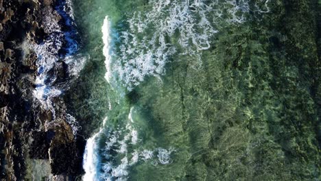 Small-foamy-waves-rolling,-drone-view-on-blue-turquoise-ocean,-breaking-waves-and-whitewash.-Sunny-day-over-the-sea.-Colourful