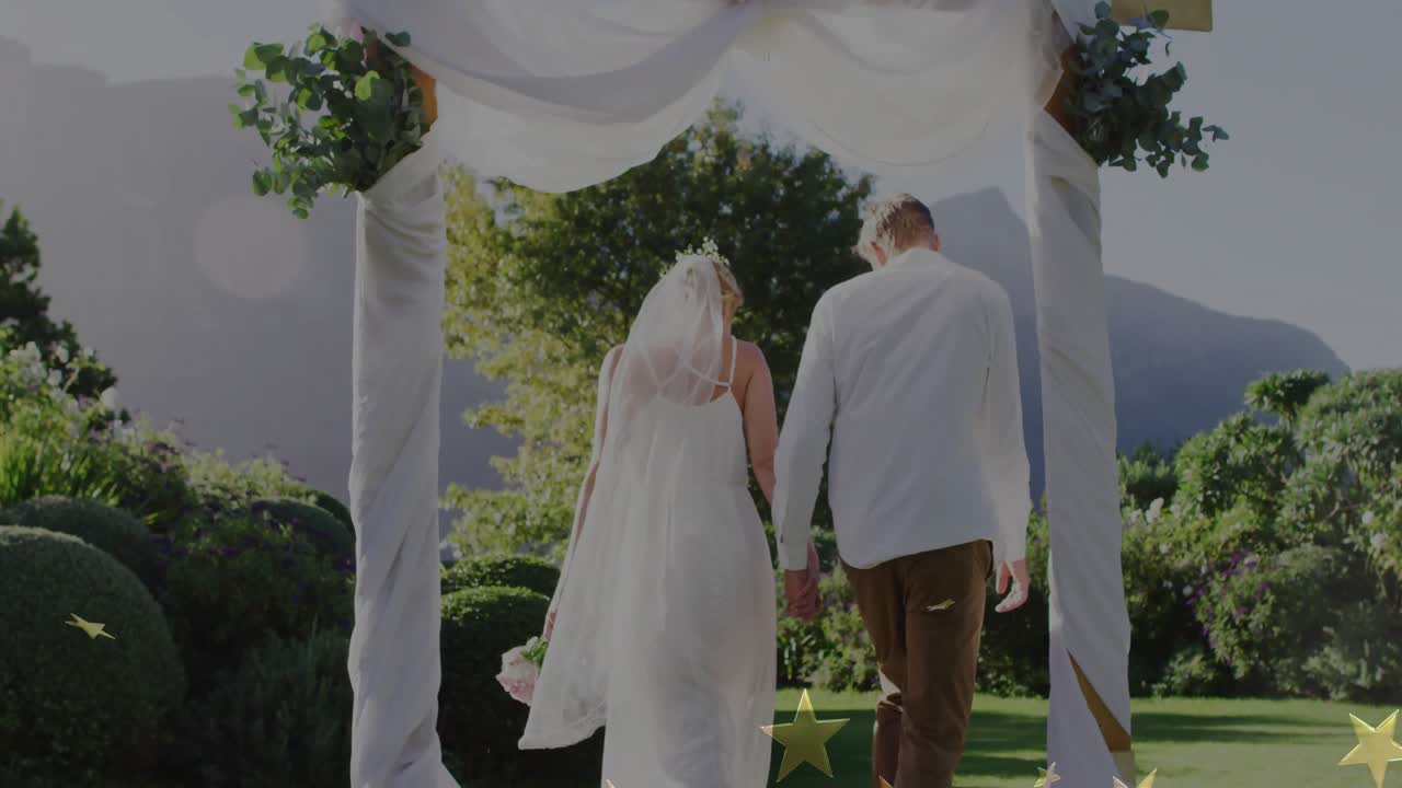 Una coppia di sposi si tiene per mano sotto un arco floreale camminando lungo un sentiero del giardino mentre icone a forma di stella segnano la loro unione.