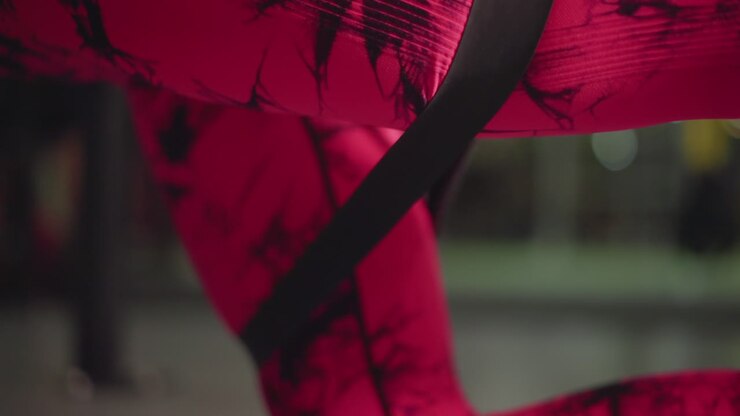 Istruttrice donna con leggings rosa che usa una fascia avvolta intorno alla coscia durante un'abduzione dell'anca con fascia, sfondo di palestra, dimostrazione concentrata dell'allenatore, ripetizioni ritmiche controllate, enfasi sull'attivazione dei glutei e sulla forma.