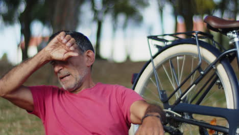 senior man sitting on lawn next to bike in summer park