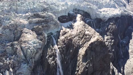 Paralax-Aéreo-De-Un-Gran-Acantilado-Con-Una-Cascada-De-Agua-Helada-Derretida-En-Los-Alpes-Suizos