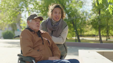 senior man in wheelchair and caregiver on walk in park
