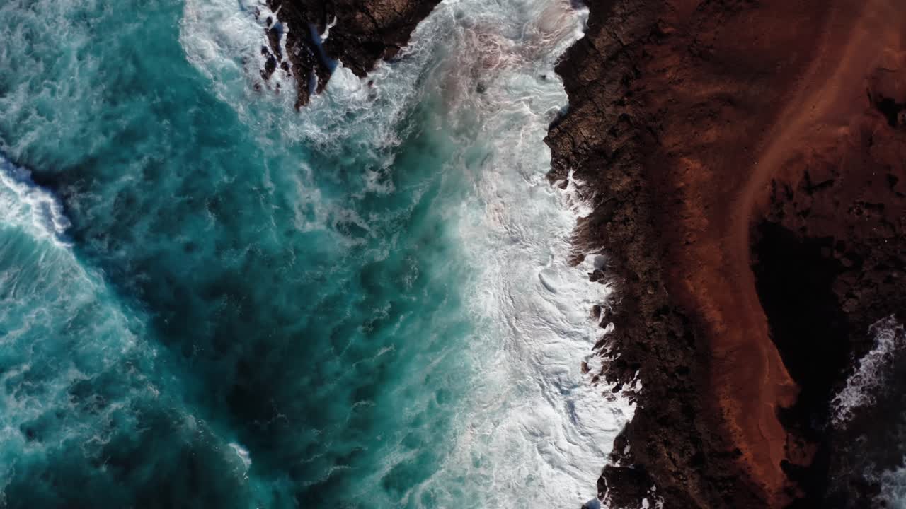 Letecký pohled shora z dronu na oceánské vlny tříštící se o útesy na Lanzarote, na Kanárských ostrovech.