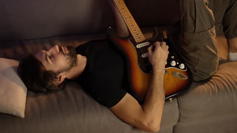 hombre componiendo música en la guitarra mientras está acostado en el sofá