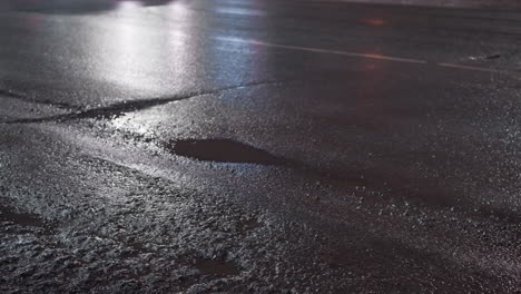 close-up view of a wet road at night, showcasing light reflections on the glistening surface with three cars driving by