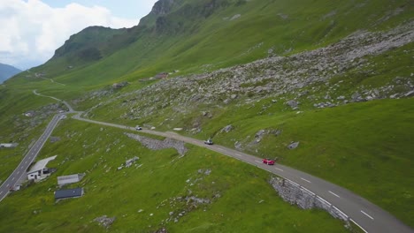 Luftwagen-In-Fahrzeugen,-Die-Tagsüber-Auf-Einer-Asphaltierten-Straße-Im-Grünen-Klausenpass-Berghang-In-Der-Nähe-Von-Kleinen-Hütten-Fahren,-Schweizer-Alpen