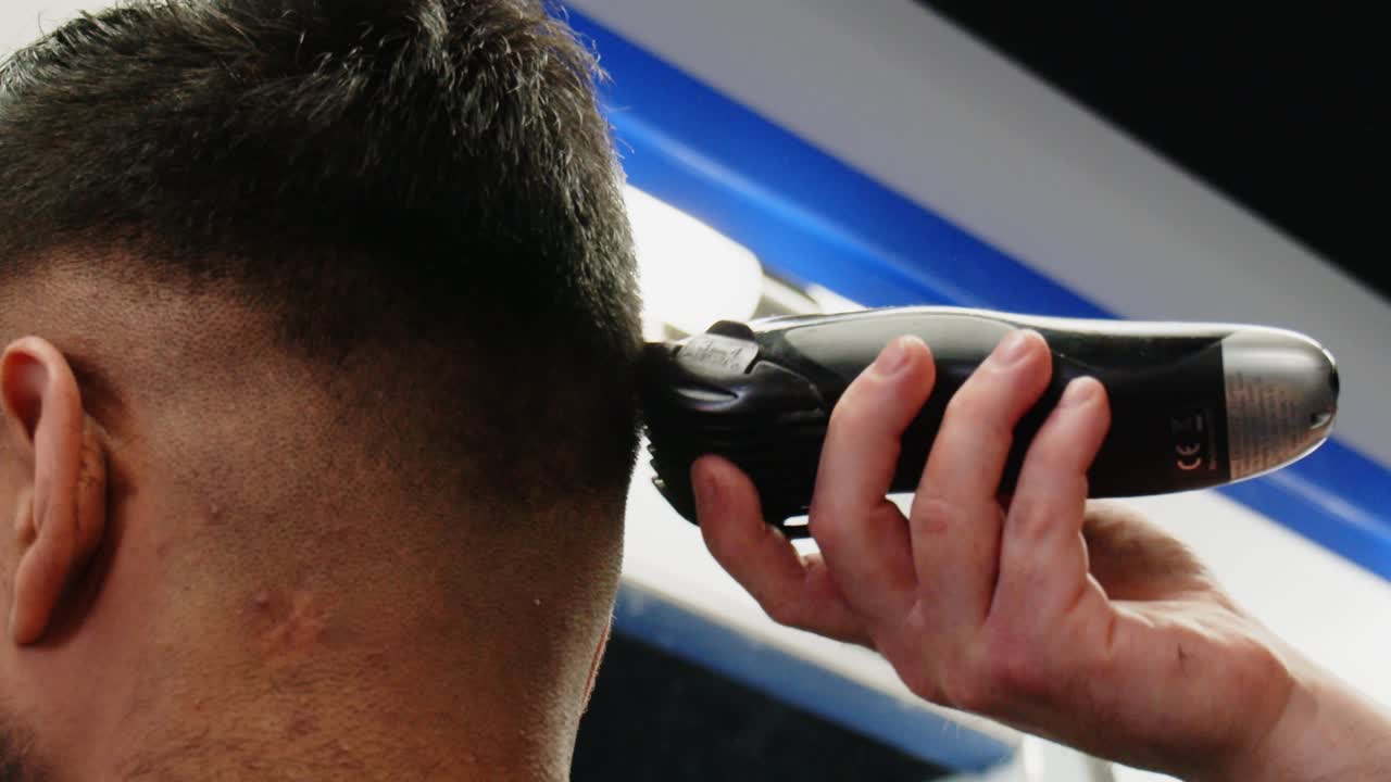 una mano blanca zumbando por la parte posterior del cabello de un hombre con cortapelos