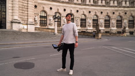 a rotating shot of a young filmmaker holding a heavy camera in an old city