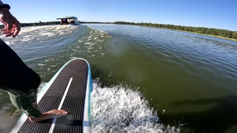 surfer on longboard in wave behind boat