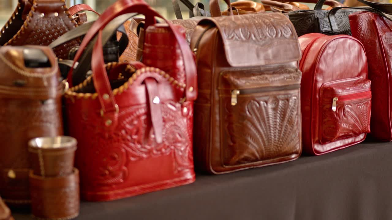 A large exhibition of genuine leather items in Paraguay, handcrafted with brown and red leather, including wrapped thermoses. The leather is carved with patterns and figures