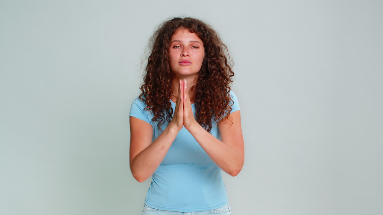 Woman humorously folding hands praying begging asking please gesture hopeful emotional reaction