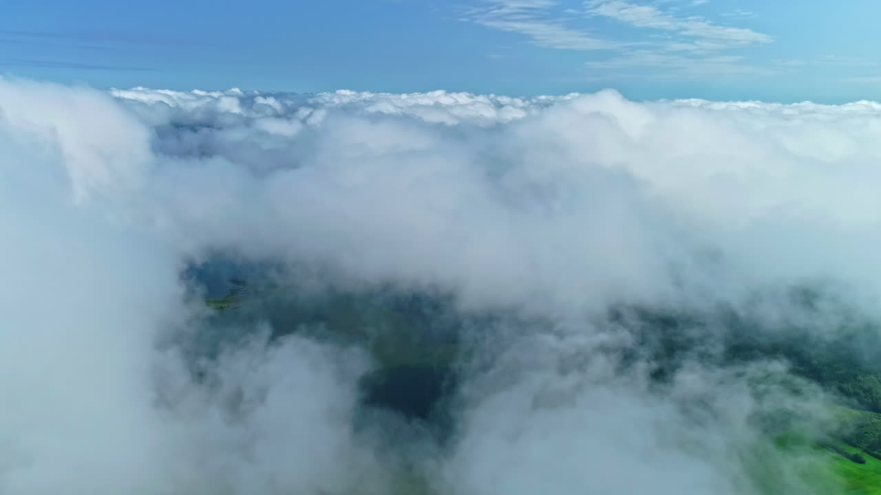 Aerial dolly of misty clouds over a lush forest landscape, with blue sky above and shadows on forest landscape below