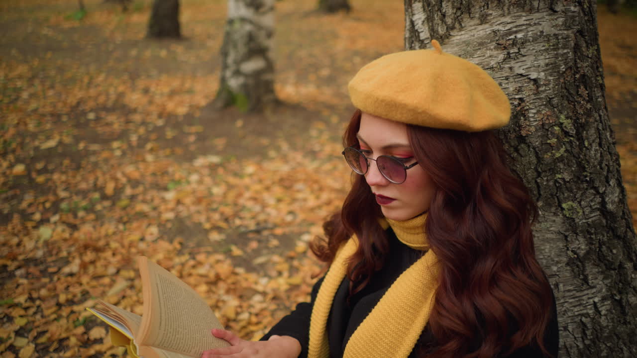 mujer pensativa con boina amarilla y silenciador lee un libro, volviendo páginas en un entorno tranquilo, rodeada de hojas doradas de otoño, disfruta de la tranquila soledad