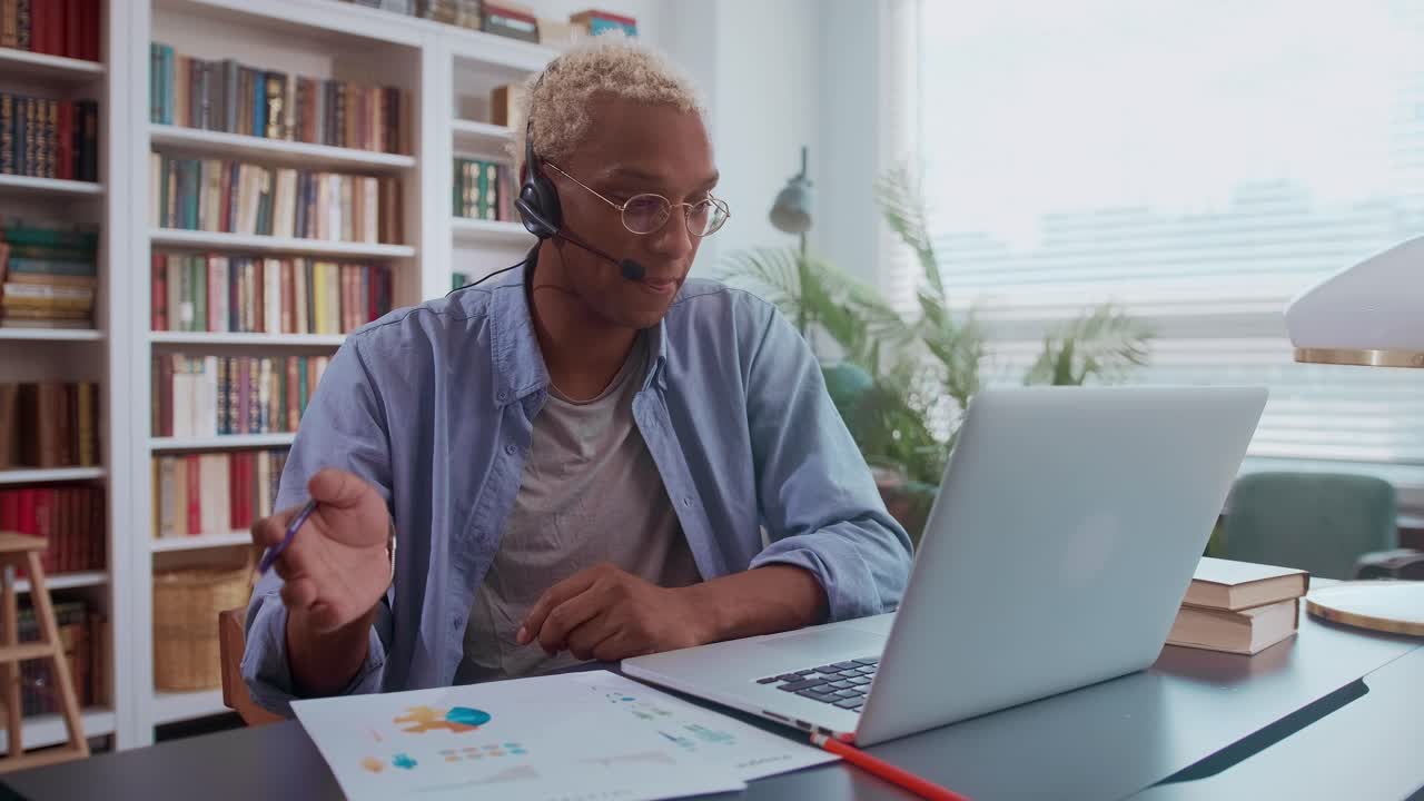 Serious darkskinned man is talking on headset and making notes in documents
