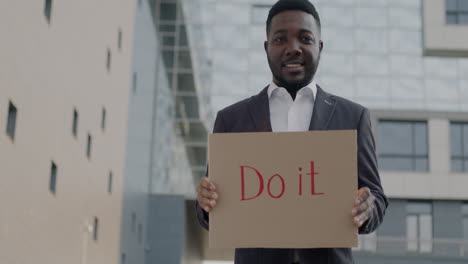 man holding a cardboard sign saying 'do it'