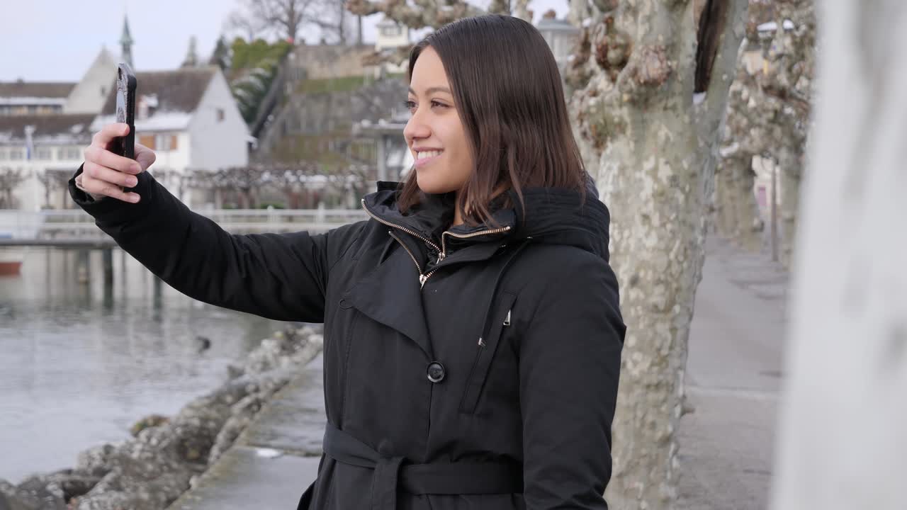 Young female model taking selfies on vacation in small wintry town on the bank of a river