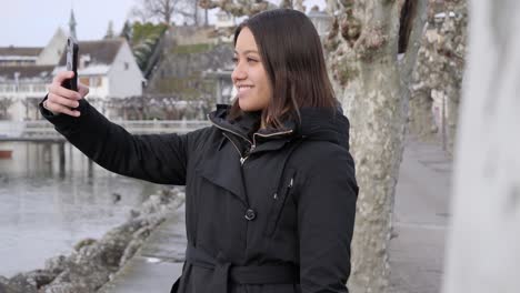 young female model taking selfies on vacation in small wintry town on the bank of a river