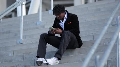 joven hombre de negocios africano sentado en las escaleras un mensaje de texto en su teléfono celular