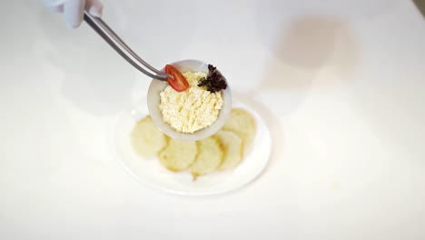hand in white glove holding kitchen tongs and decorating tasty dish with vegetables. delicious food on plates for special day over the white tablecloth. close-up