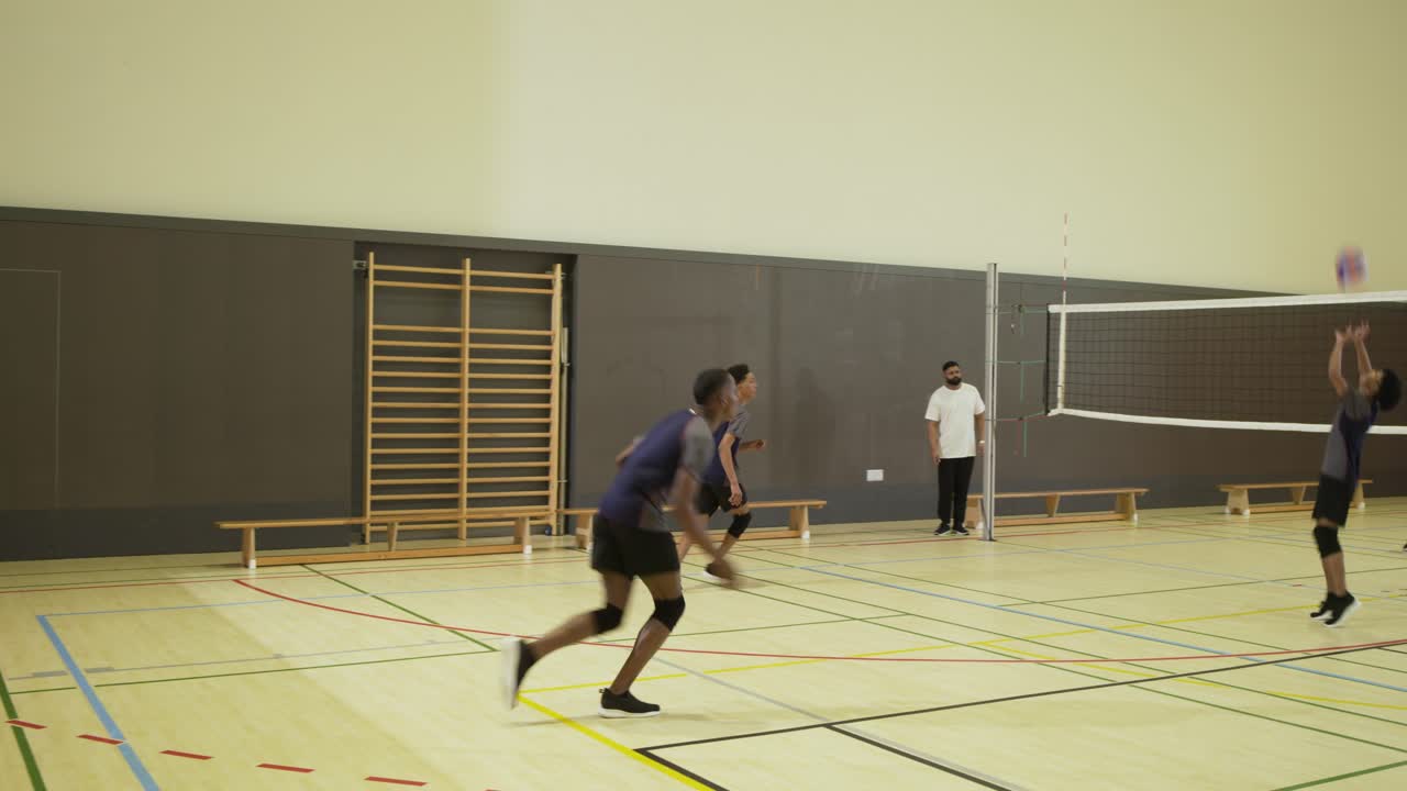Two opposing male teams competing, serving, passing, diving on school gym with purple volleyball