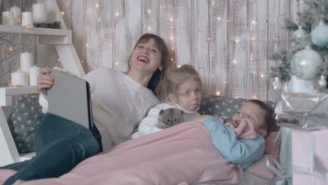 mom in white sweater laughs at childrens cuteness on bed