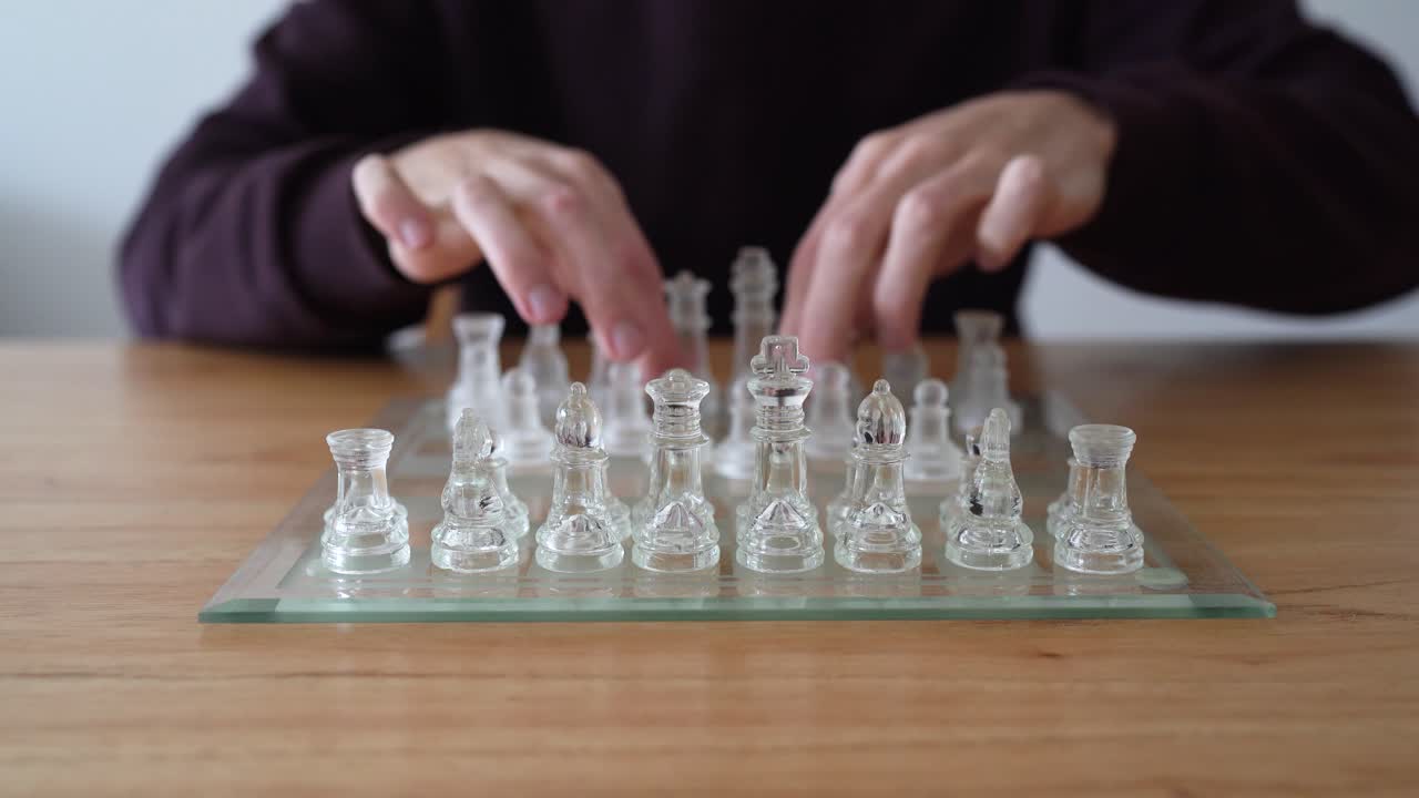 Person Arranging Transparent Glass Chess Pieces On Glass Chessboard, Preparing For Game. closeup shot