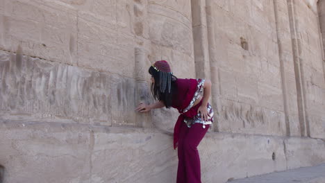 woman in traditional costume touching hieroglyphic wall at dendera temple, egypt