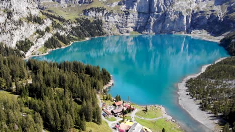 Sobrevuelo-Aéreo-Junto-Al-Lago-Oeschinensee-En-Kandersteg,-Suiza,-Con-Un-Reflejo-De-Los-Acantilados-De-Bluemlisalphorn-En-El-Agua-Turquesa