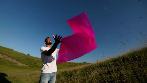 man throwing a pink fabric in a field under a clear sky