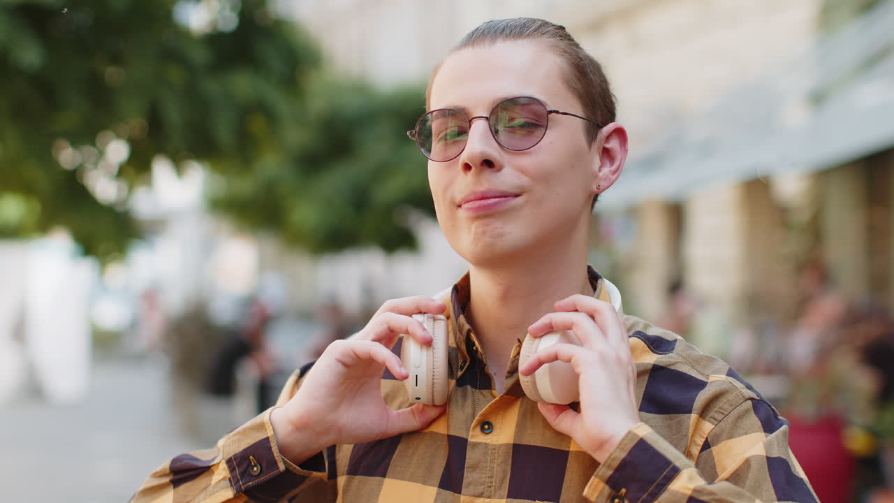 Happy smiling man listening music taking off wireless headphones looking at camera on city street
