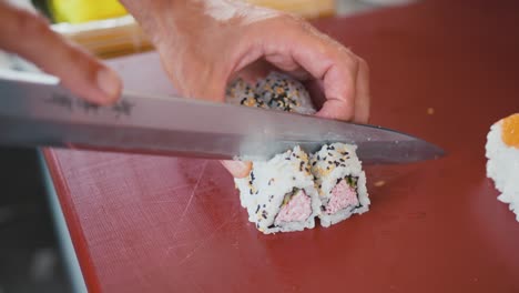 A-professional-chef-cuts-a-roll-of-sushi-into-pieces,-making-uramaki-rolls,-traditional-Japanese-cuisine