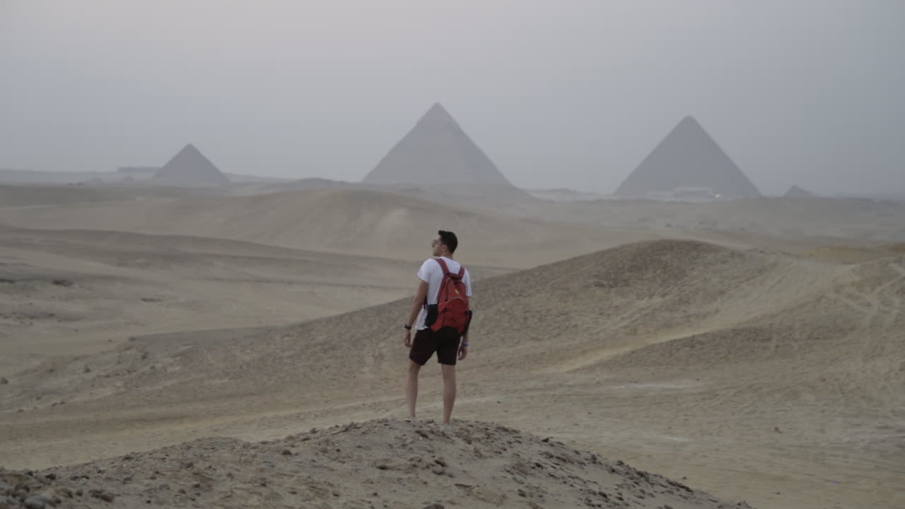 Young man standing in Egyptian desert with Giza pyramids in distance at sunset