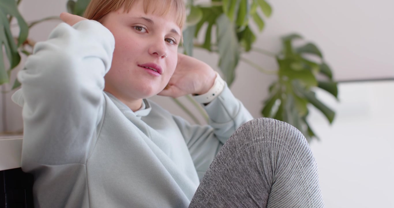 Donna che sistema una scarpa da ginnastica rosa alla caviglia, liscia i leggings su una panca bassa e guarda la telecamera.