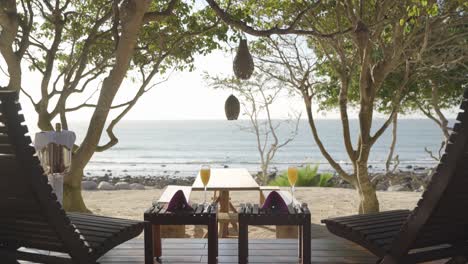 static scene from a luxury resort seeing the ocean between two lounge chairs with glasses of mimosas and bottle of champagne on the side