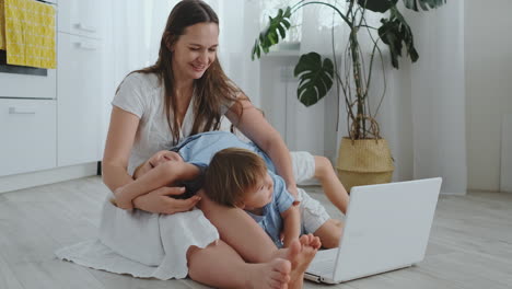 hermosa familia joven moderna acostada en el suelo en casa y haciendo algo en la computadora portátil