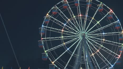 brightly-lit-Ferris-wheel-turns-in-park-against-black-sky