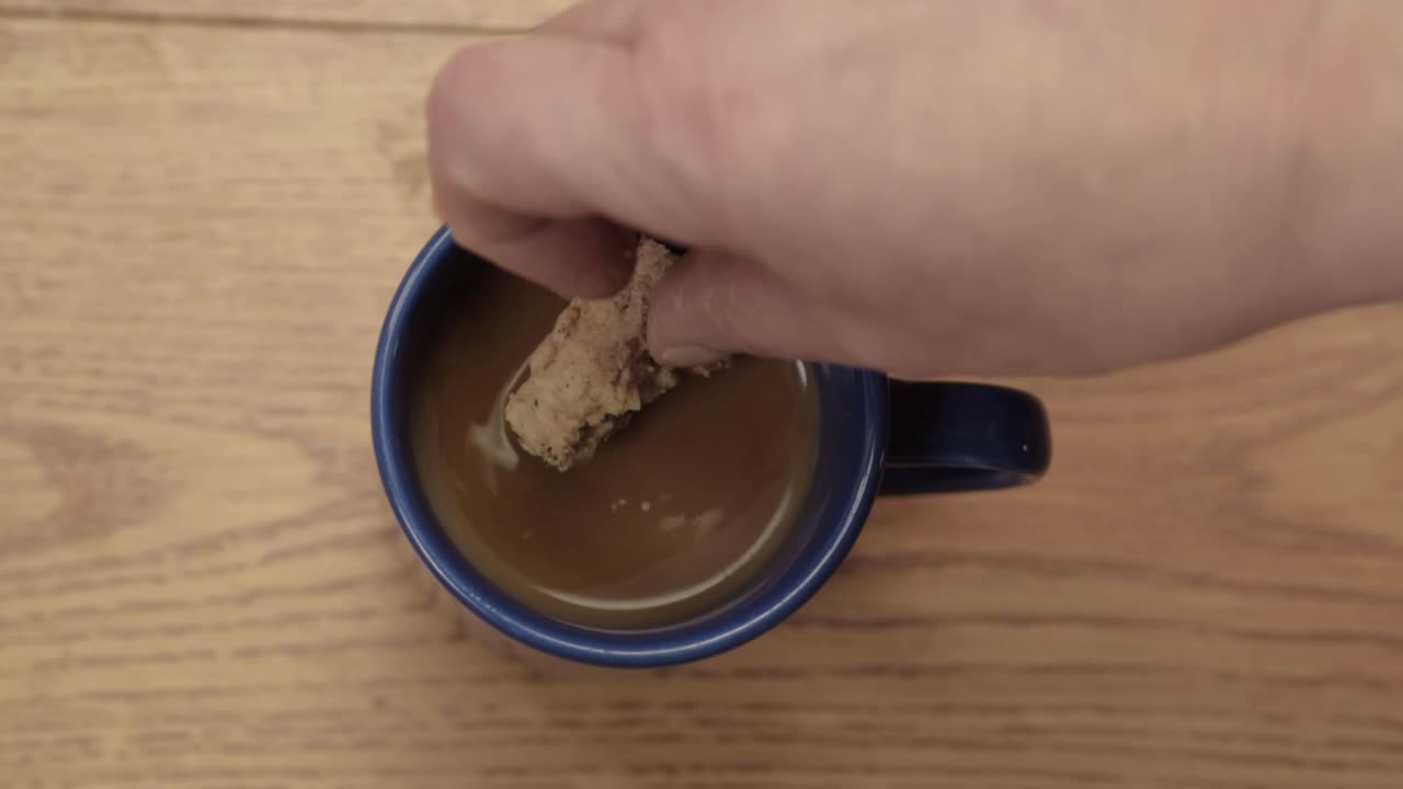 Hand dunking cookie in pot of coffee overhead close up shot