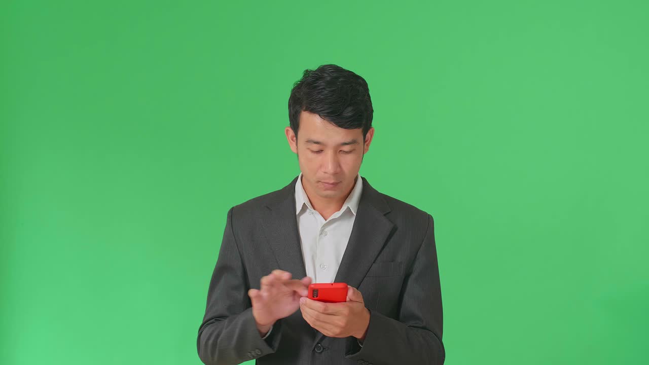 Happy Young Asian Business Man Use Mobile Phone While Standing On Green Screen In The Studio