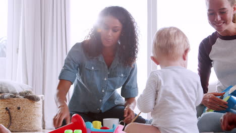 mujeres blancas y negras jugando con sus niños pequeños en casa