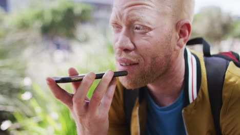 happy albino african american man with dreadlocks in park talking on smartphone