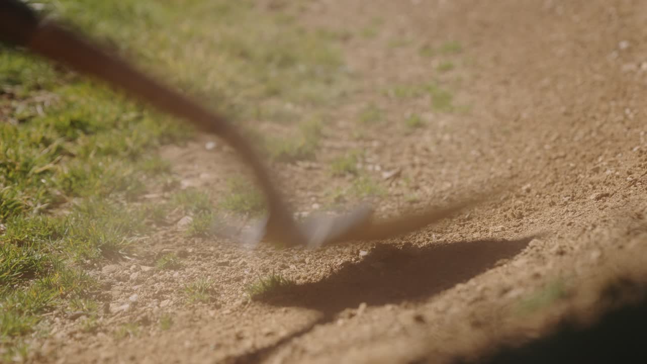 Shovel hits dry dirt on a sunny day as dust rises against a green grassy background