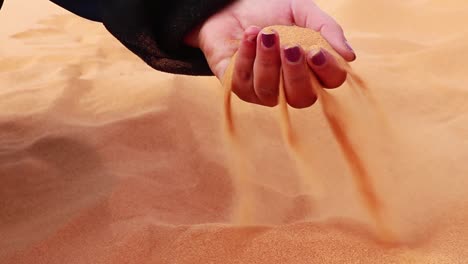 woman moving hand through desert sand, which slips through her fingers and blows away