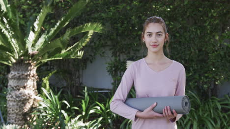 Happy-caucasian-woman-standing-with-yoga-mat-and-smiling-in-sunny-garden,-copy-space,-slow-motion