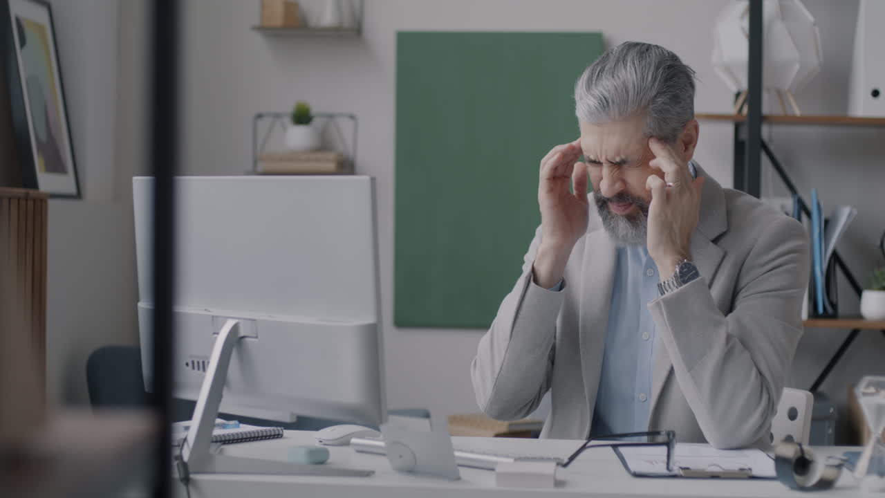 Businessman in office with headache and computer