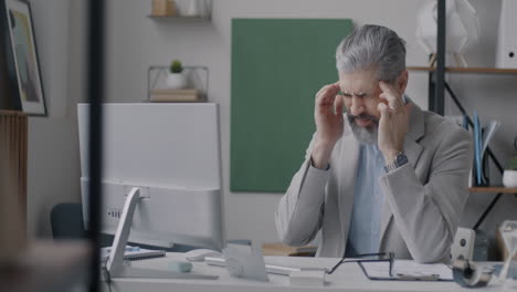 businessman in office with headache and computer