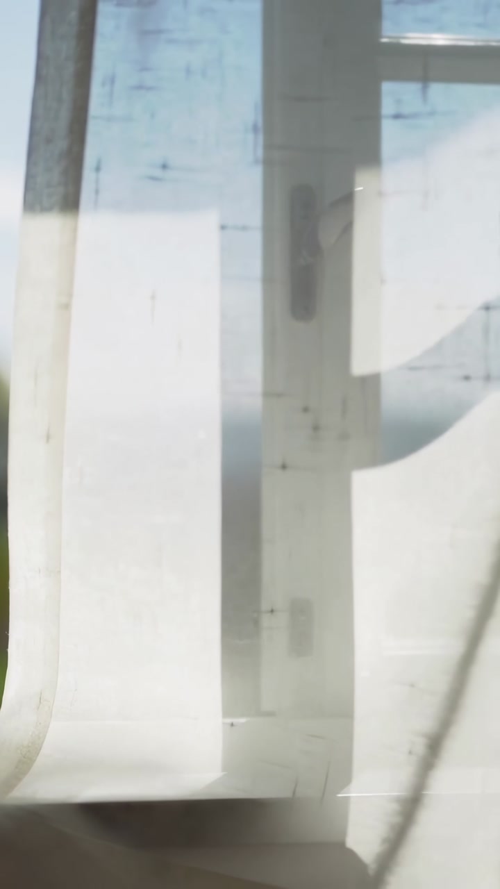 Vertical video: Billowing sheer white curtain swaying inside room by breeze at window showing latch