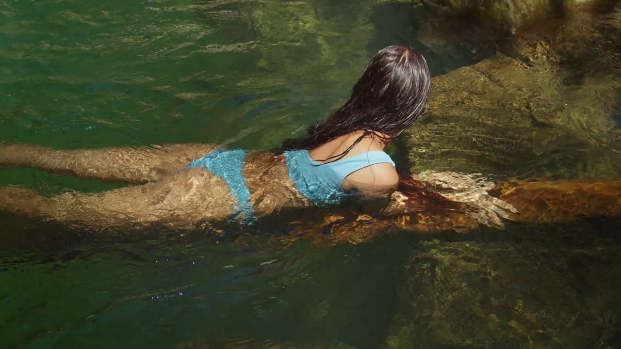 비키니를 입은 히스패닉 소녀가 폭포에 있는 웅 ⁇ 이의  ⁇ 은 물에 줄을  ⁇ 고 있습니다.