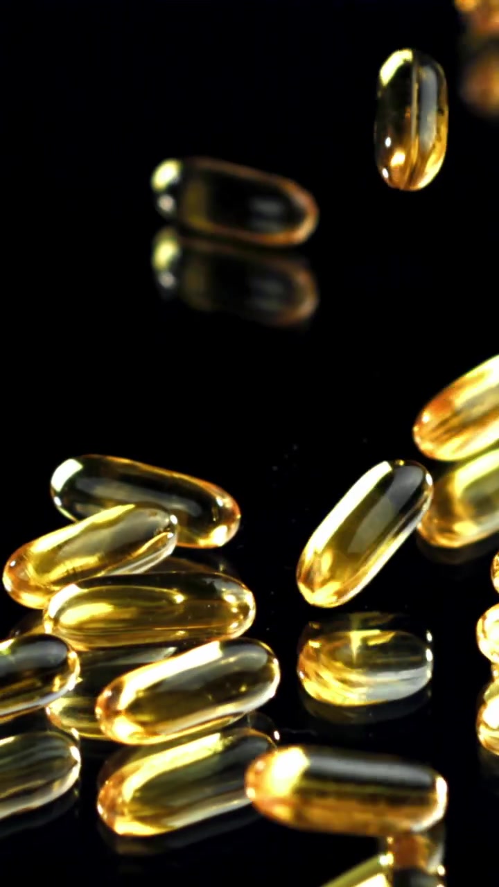 Rallentatore di capsule di gel dorate che cadono su sfondo nero.