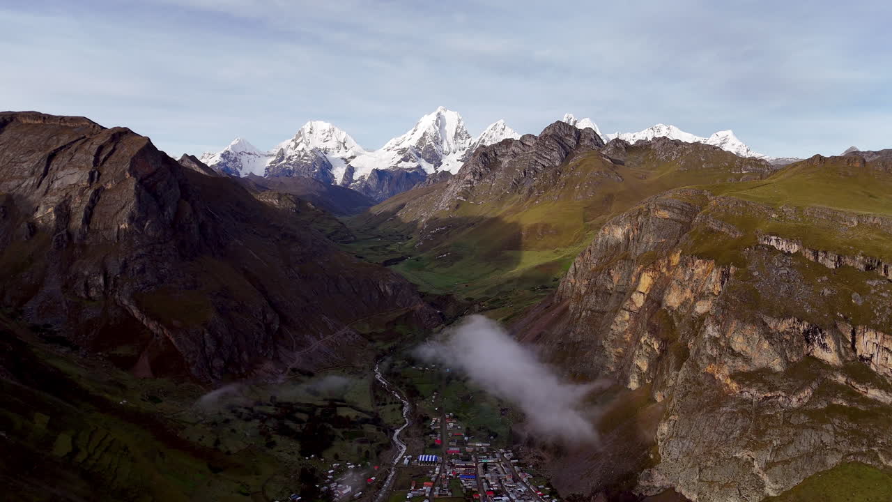 Cinematic aerial view of snowy Andes mountains in Peru with glaciers, rocky cliffs, and hidden blue alpine lake under misty clouds, dramatic landscape and natural travel destination